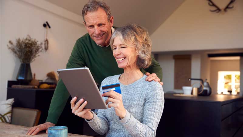 A couple at home together smiling as they look at something on a tablet together