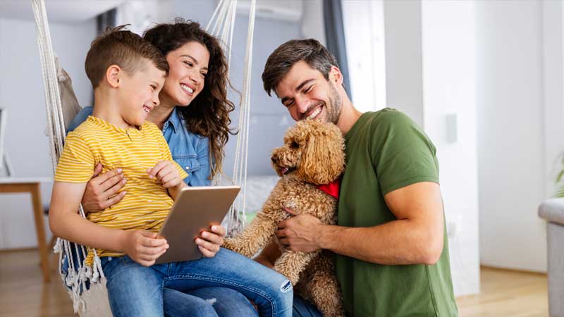 A couple with a young child holding a tablet play with a golden doodle puppy