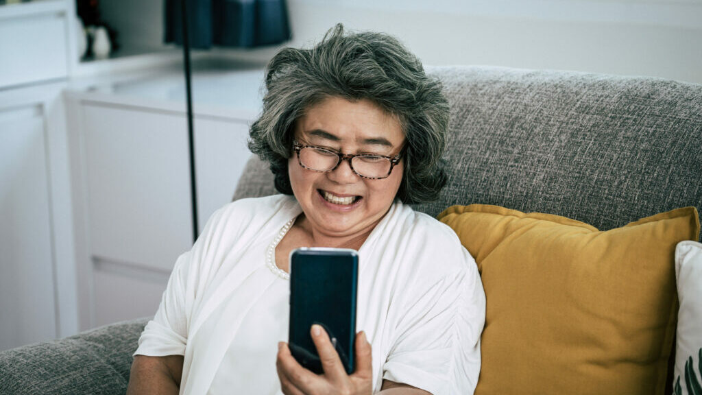 Femme à la maison dans son salon souriant alors qu'elle a un appel vidéo avec un ami sur son téléphone portable